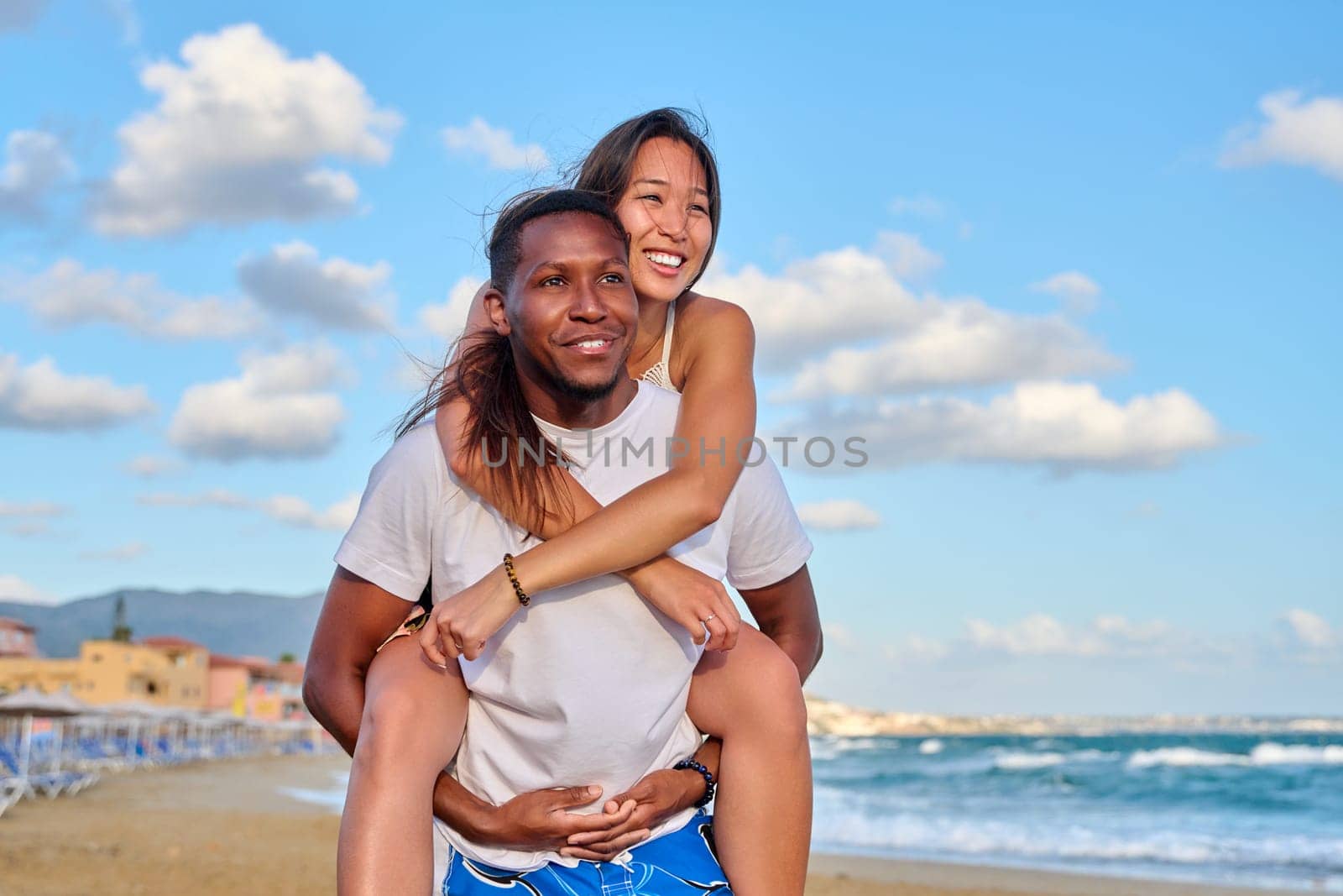 Happy young beautiful couple having fun on beach. Afro american asian couple laughing enjoying vacation in seaside nature. Multicultural, multiethnic family, relationships, togetherness, lifestyle