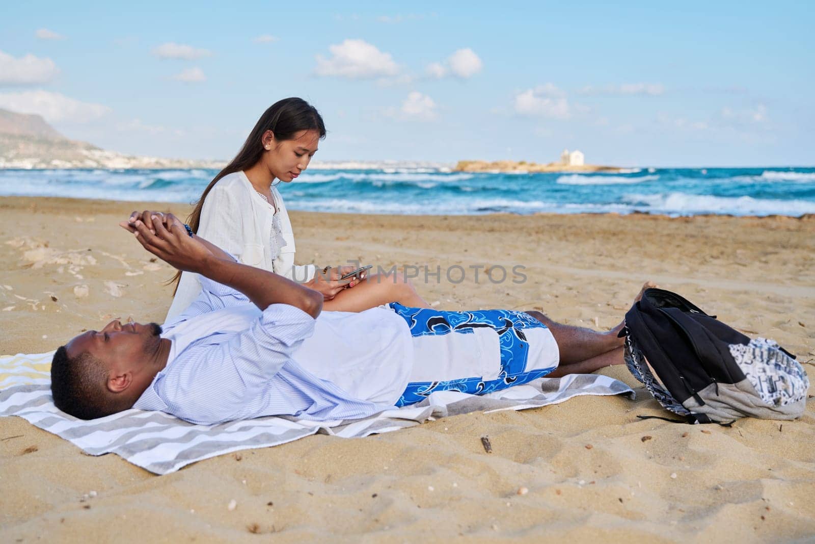 Young couple relaxing on the beach, lying sitting on the sand with smartphones. Summer autumn vacation together, lifestyle. technology, family concept