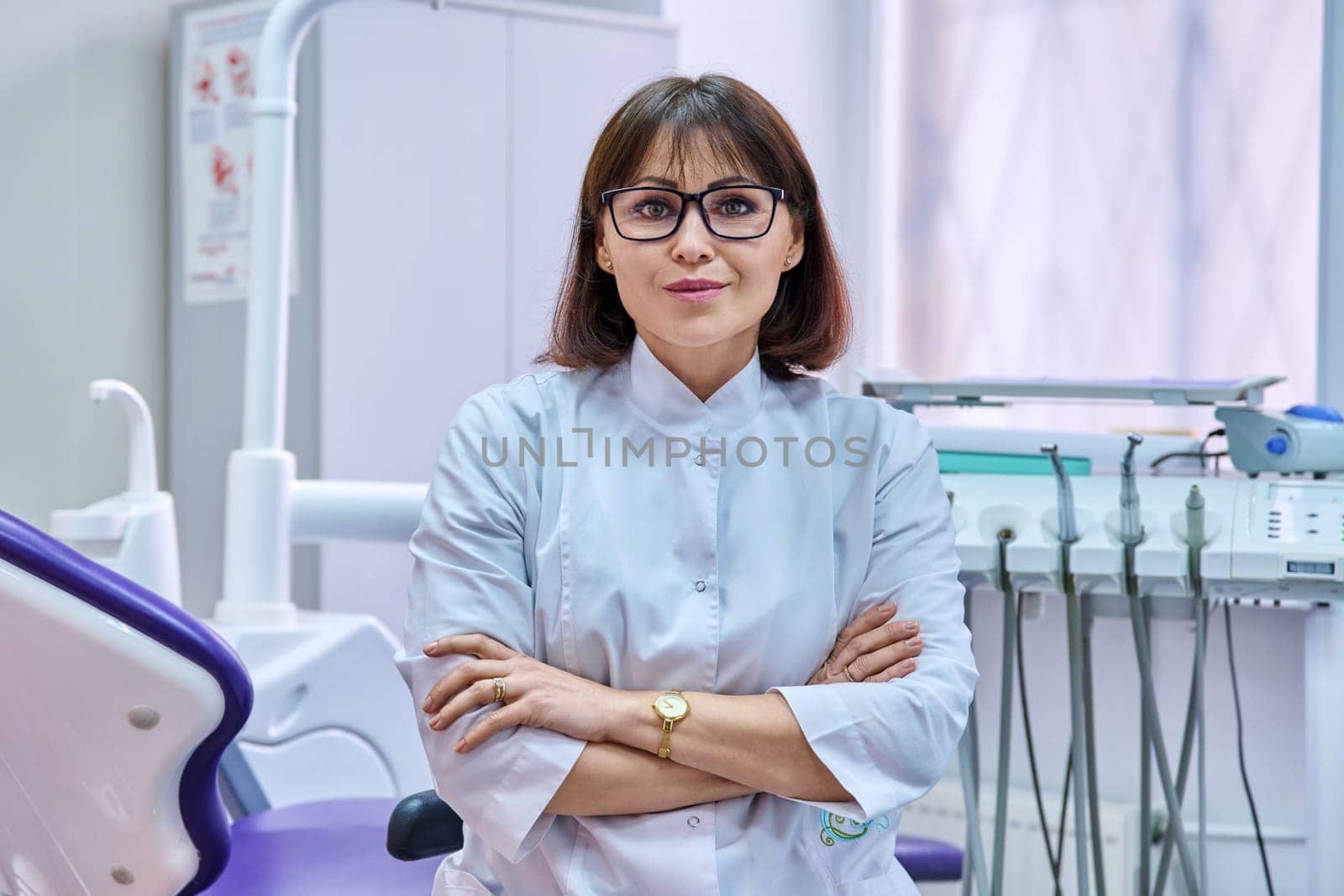 Portrait of confident female dentist in office looking at camera. Middle aged female doctor with crossed arms. Dentistry, medicine, health care, profession, stomatology concept