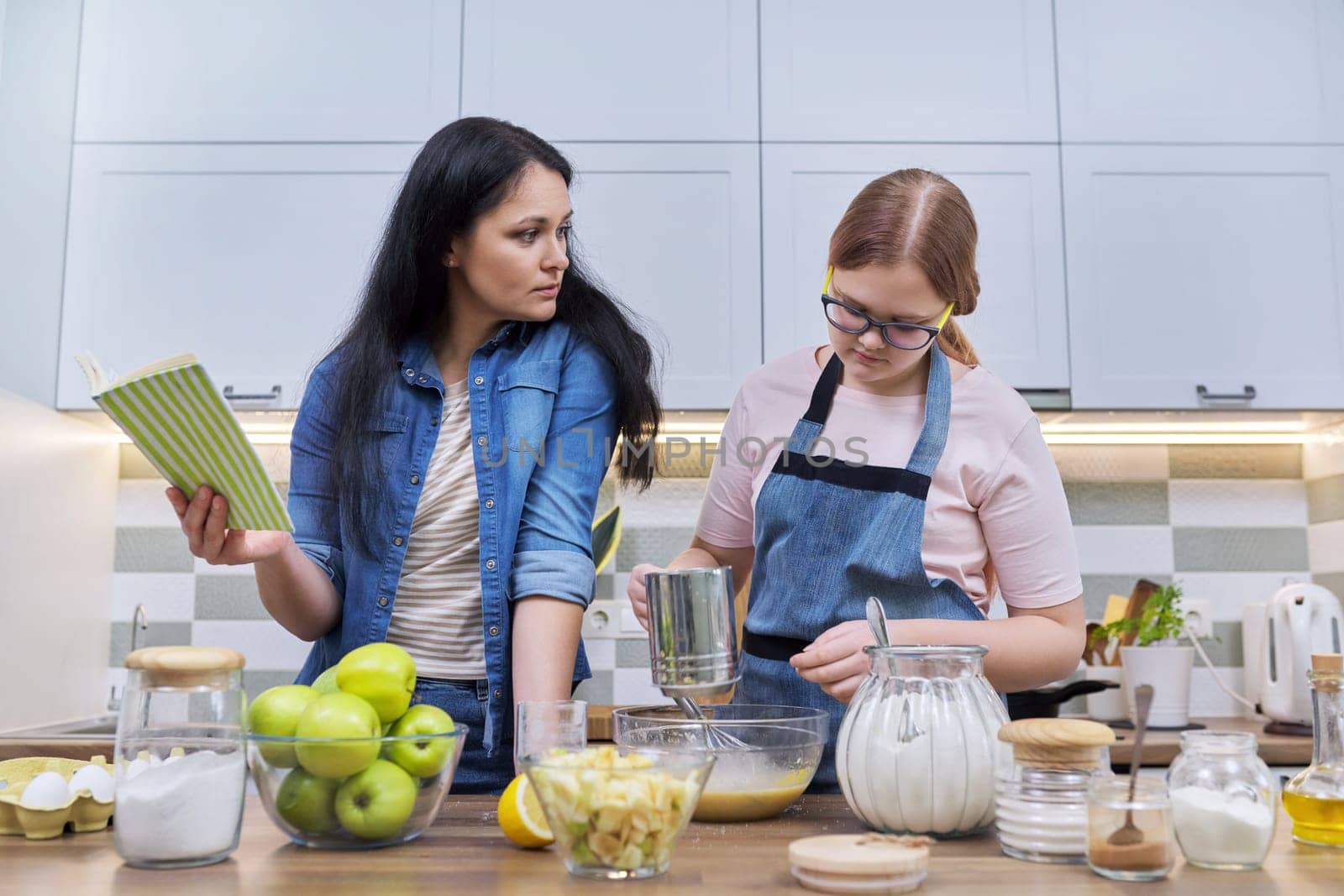 Mother and teenage daughter cooking at home in kitchen. Mom and girl making apple pie together, talking smiling. Relationships, communication parent teenager, healthy homemade food, family concept