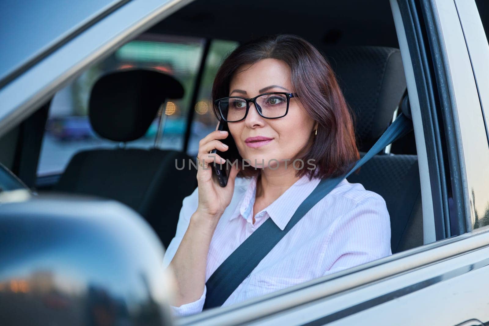 Confident female driver with smartphone driving a car. Serious beautiful female in glasses, lifestyle, transportation, people 40s age concept