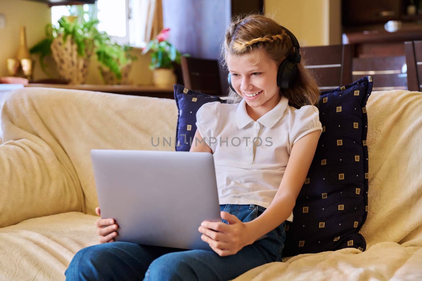 Girl child in headphones resting at home on sofa using laptop by VH-studio