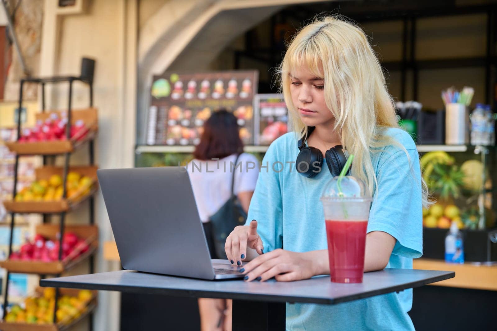 Young woman in outdoor cafe with fruit fresh juice using laptop by VH-studio