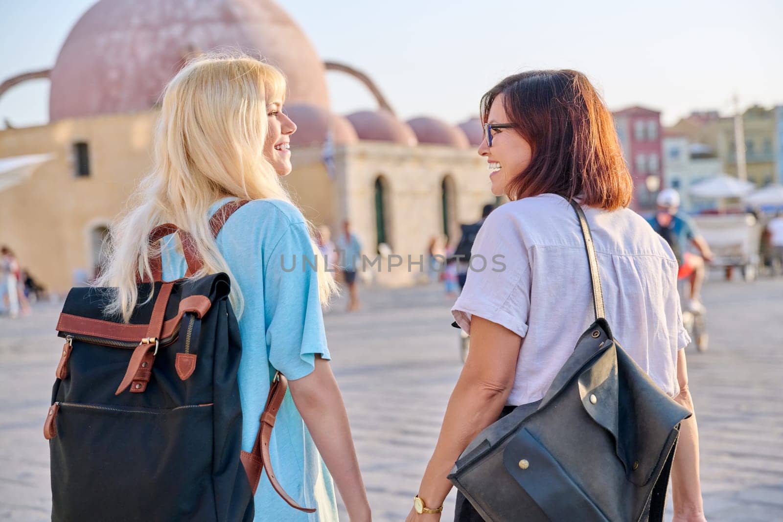 Mother and teenage daughter walking together in the old tourist town, back view by VH-studio