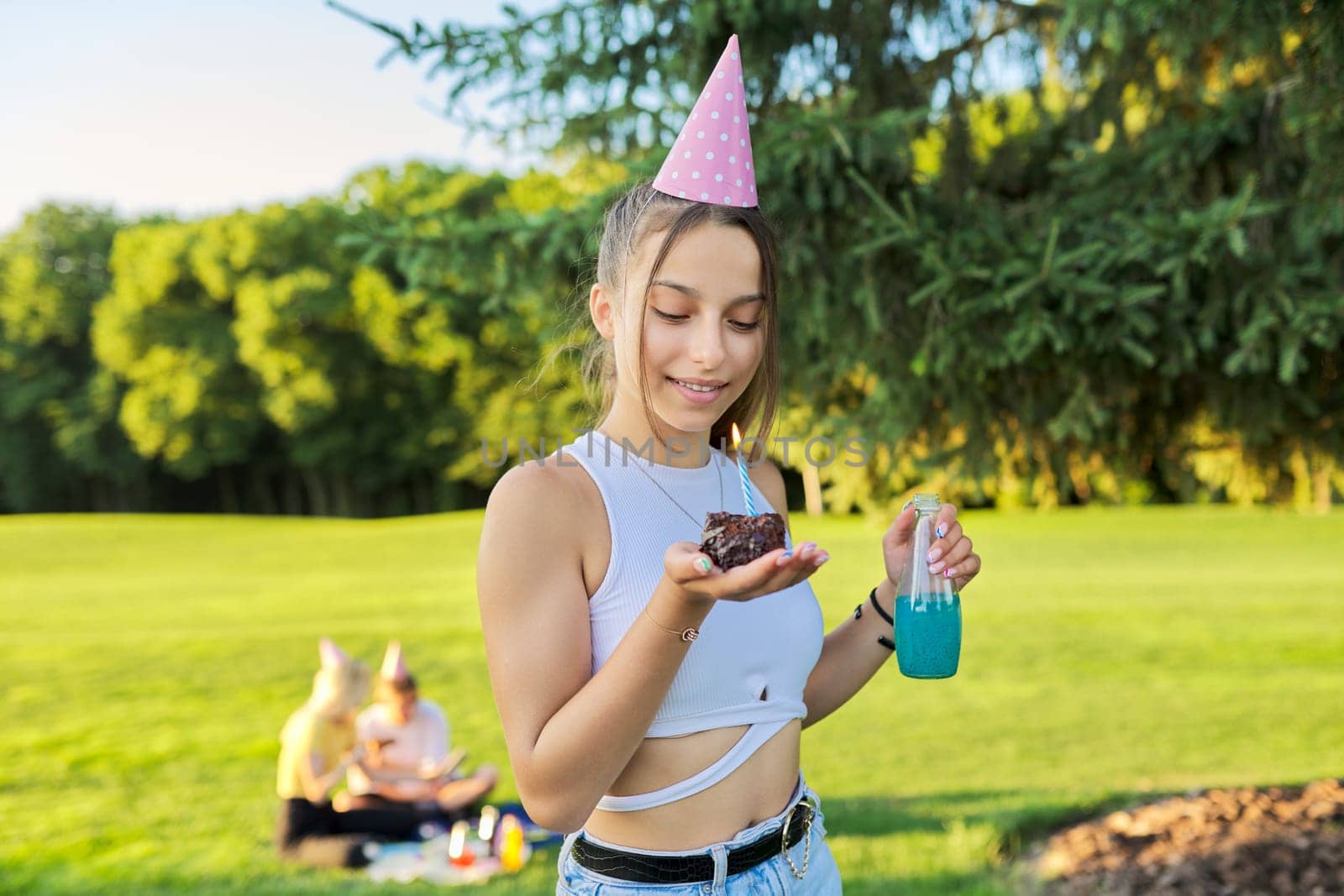 Birthday, teenage girl in festiv hat with cake and candle at outdoor party. Picnic in nature, happy having fun female. Adolescence, holiday, birthday, celebration, age concept