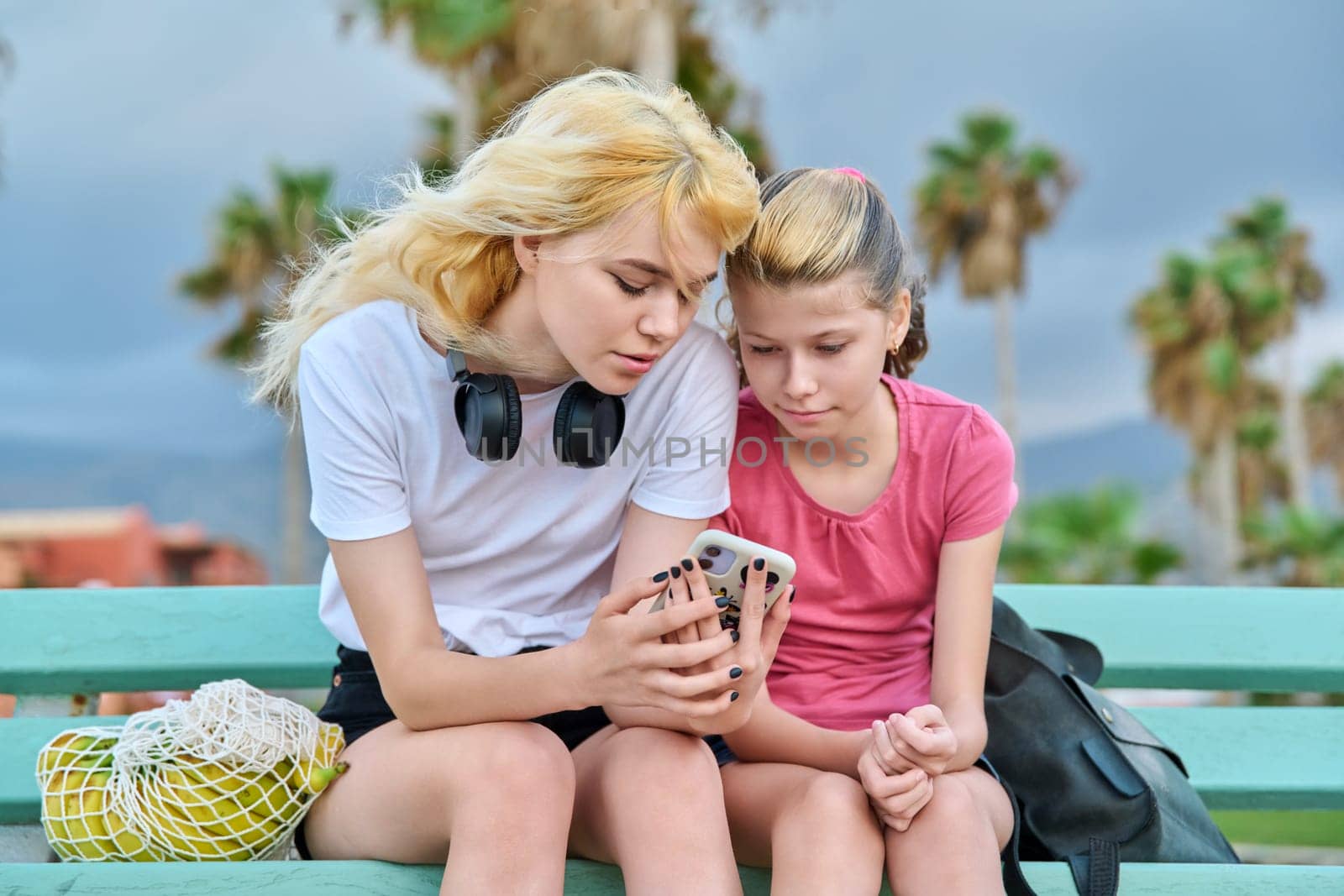 Two girls sisters, teenage and preteen look at a smartphone by VH-studio