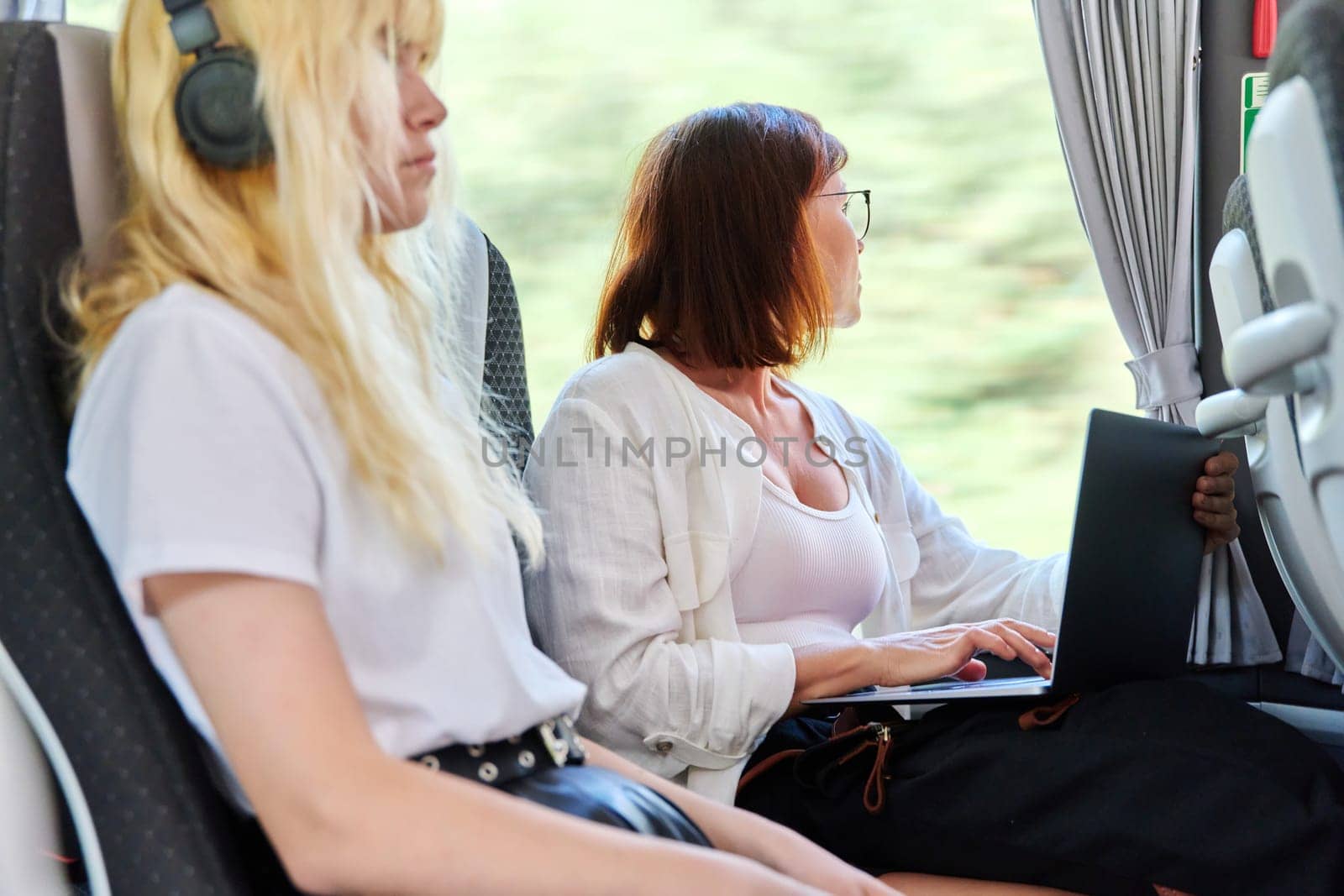 Middle-aged woman in bus using laptop. Female on bus ride working on laptop. Lifestyle, technology, travel, freelance, remote work study concept