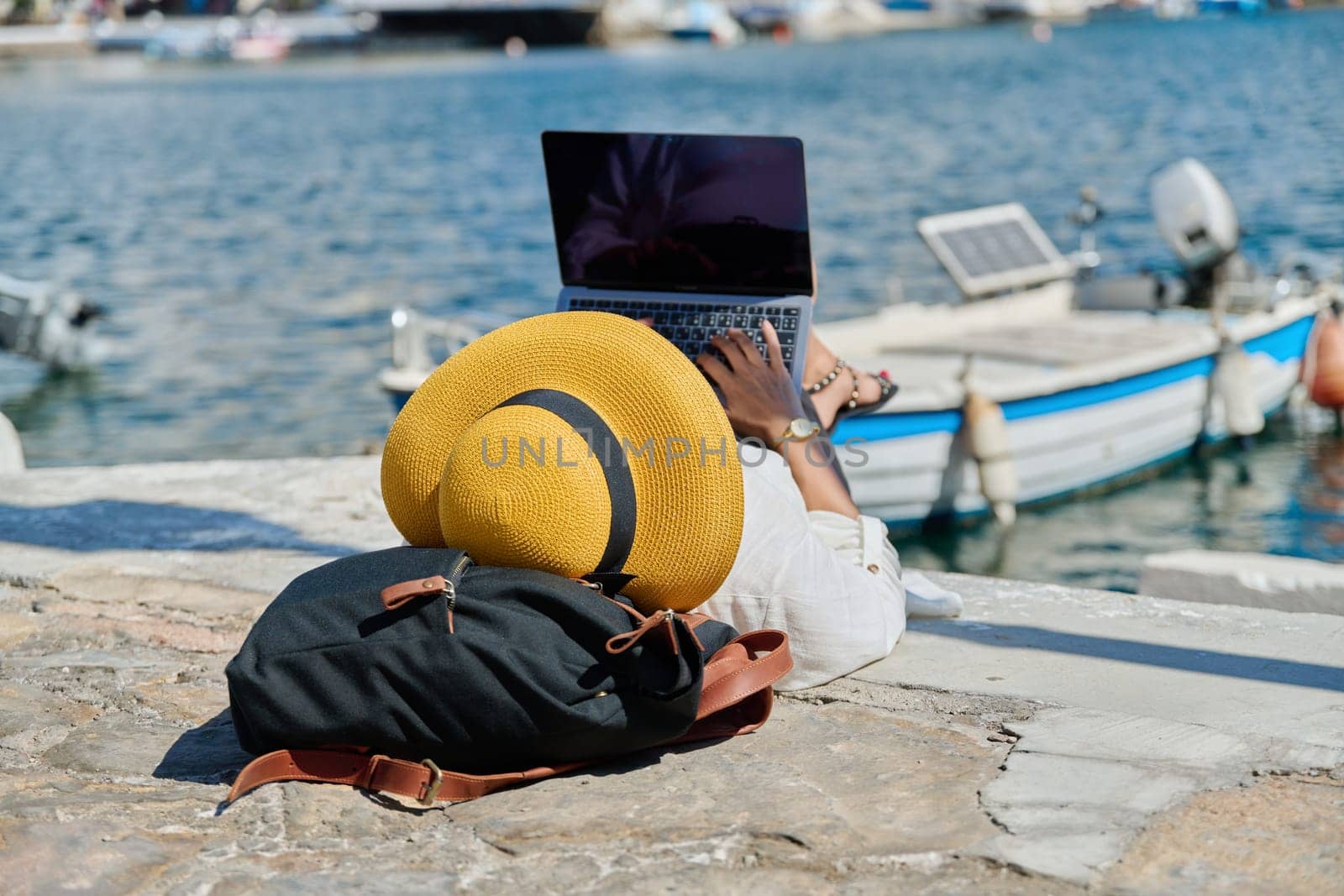 Woman in hat typing on laptop, water bay boat background. Remote work, freelance, tourism, travel, business and entrepreneurship, technology concept