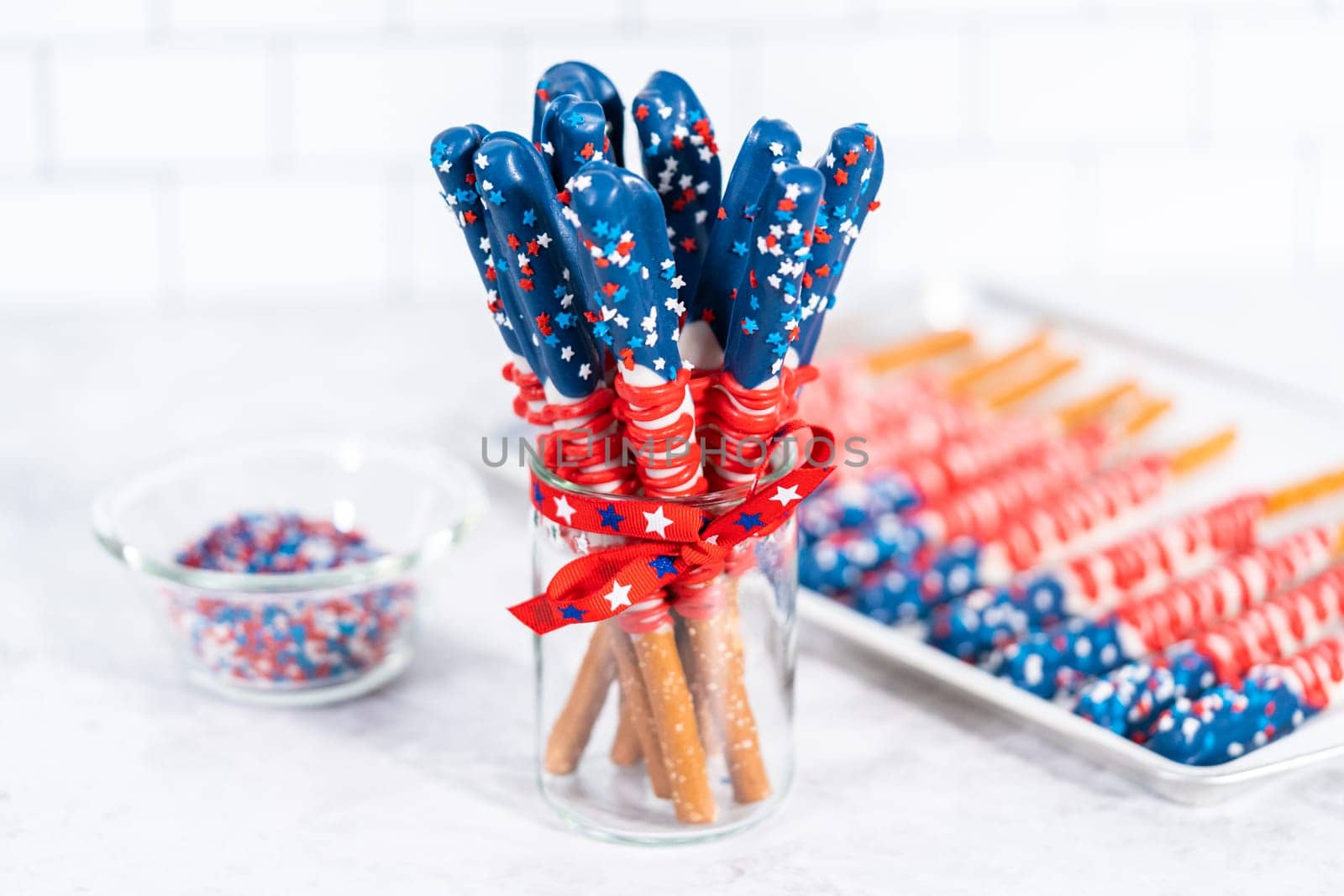 Homemade chocolate-covered pretzel rods decorated like the American flag in a glass jar.