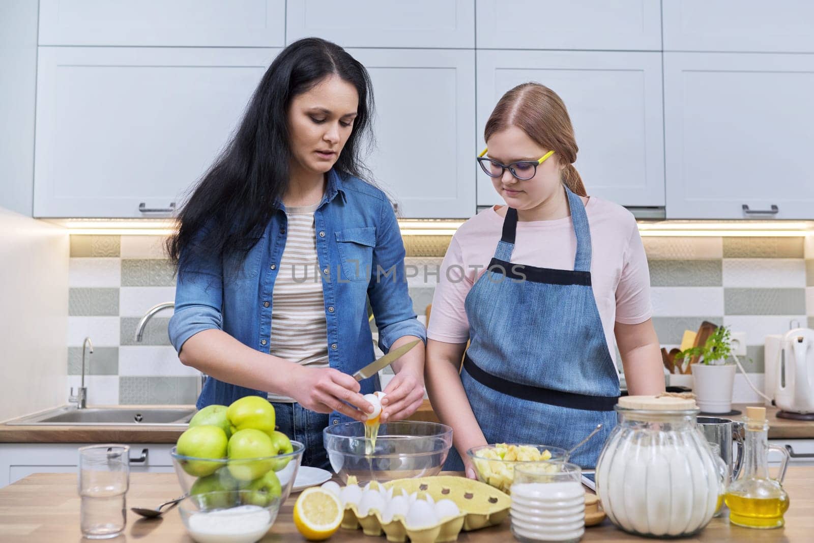 Mother and teenage daughter cooking at home in the kitchen. by VH-studio