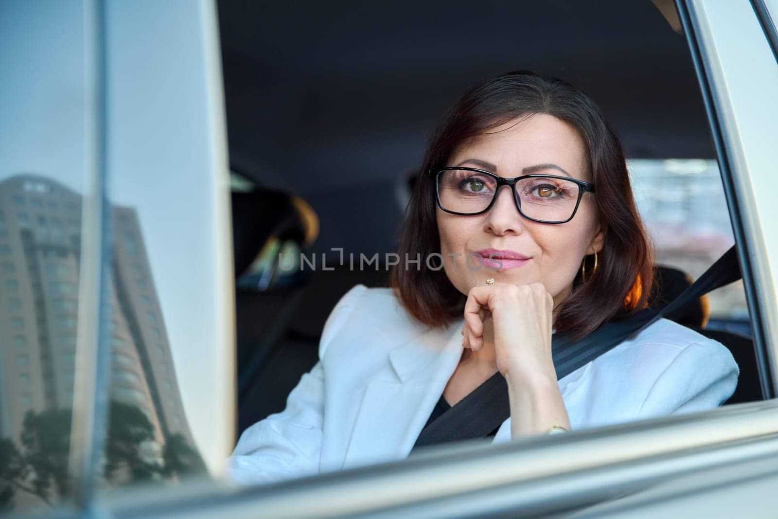 Portrait of business elegant middle-aged woman in car in back passenger seat by VH-studio