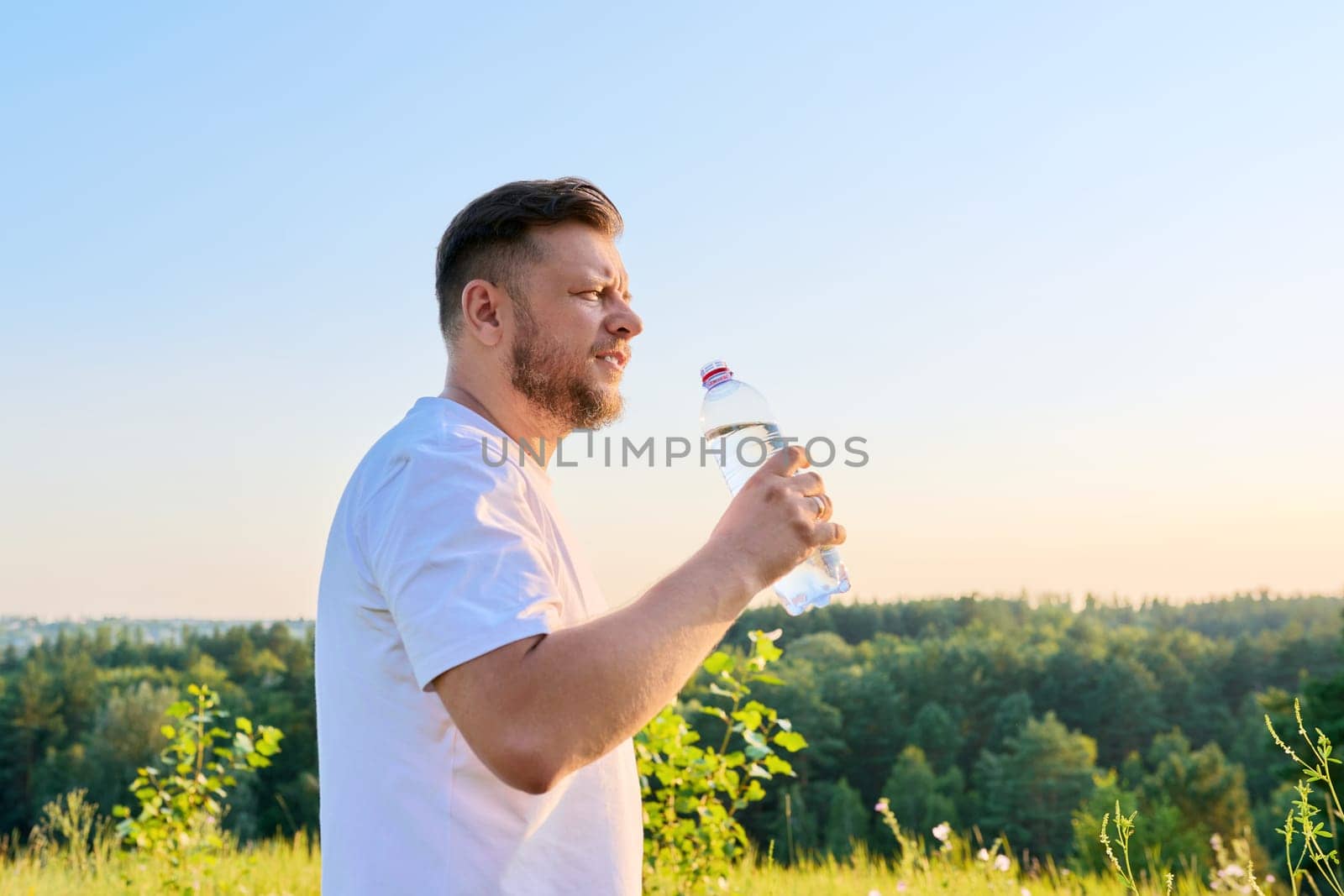 Bearded middle aged man drinking water from a bottle on a hot sunny summer day. by VH-studio