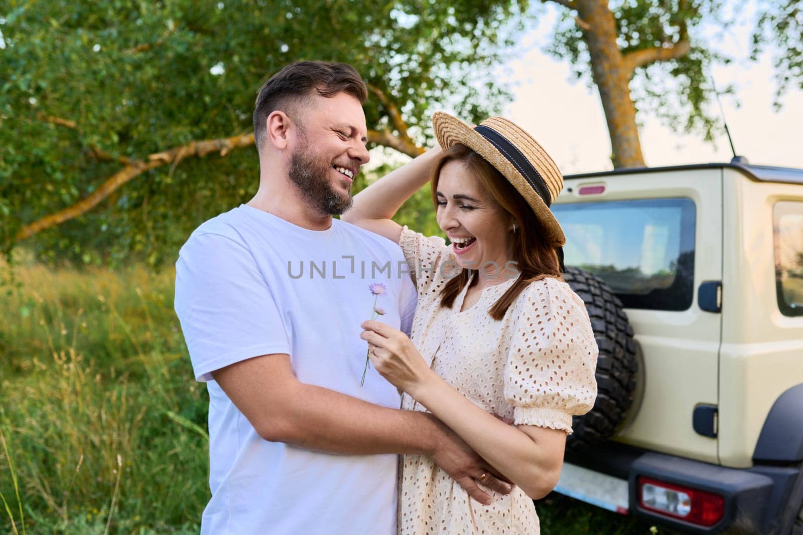 Love and romance of middle-aged couple. Happy hugging man and woman near car, summer nature wild meadow background. Relationship, holiday, date, trip, journey, weekend, family, people 40s concept