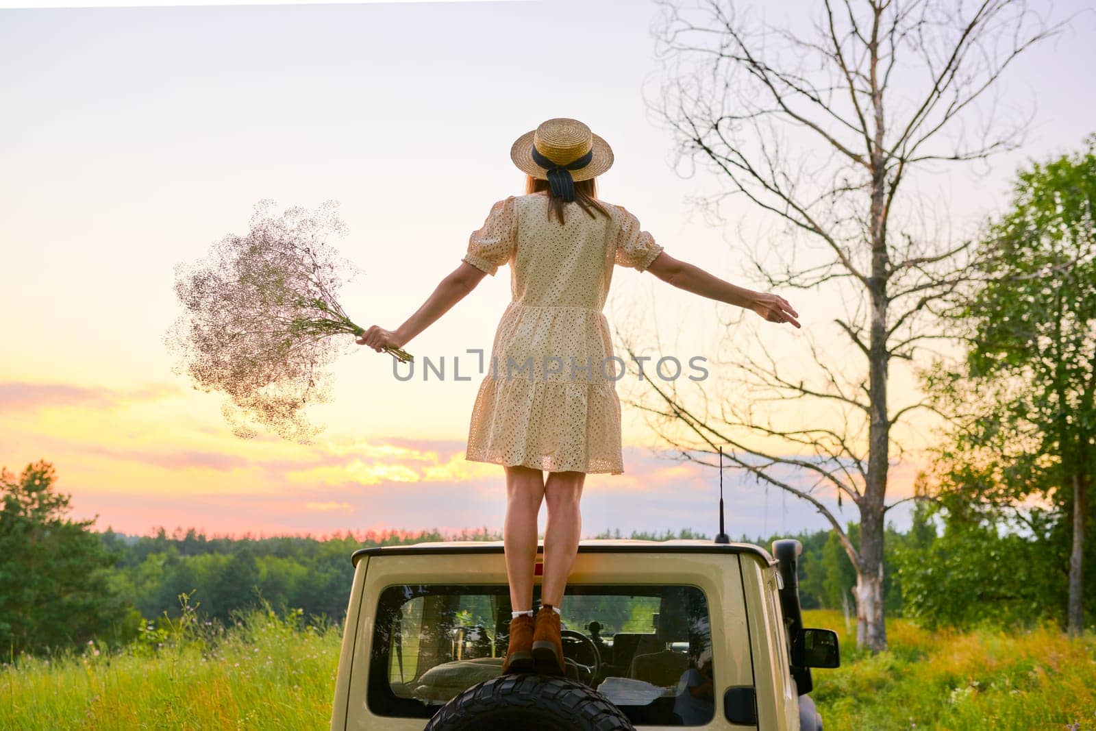 Beautiful woman in straw hat dress with bouquet of flowers back on the roof of car by VH-studio