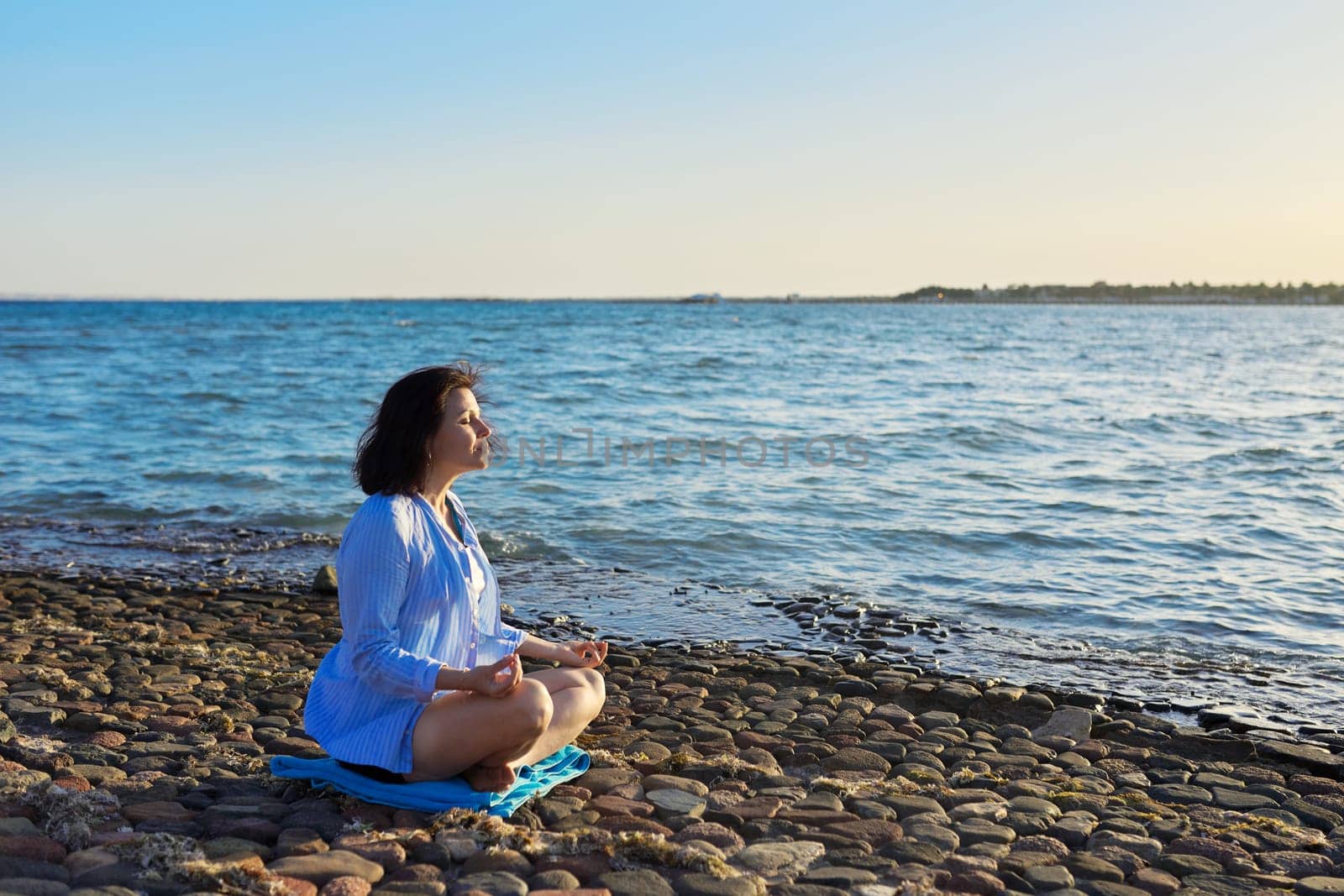 Mature woman sitting in lotus position meditating on the beach. by VH-studio