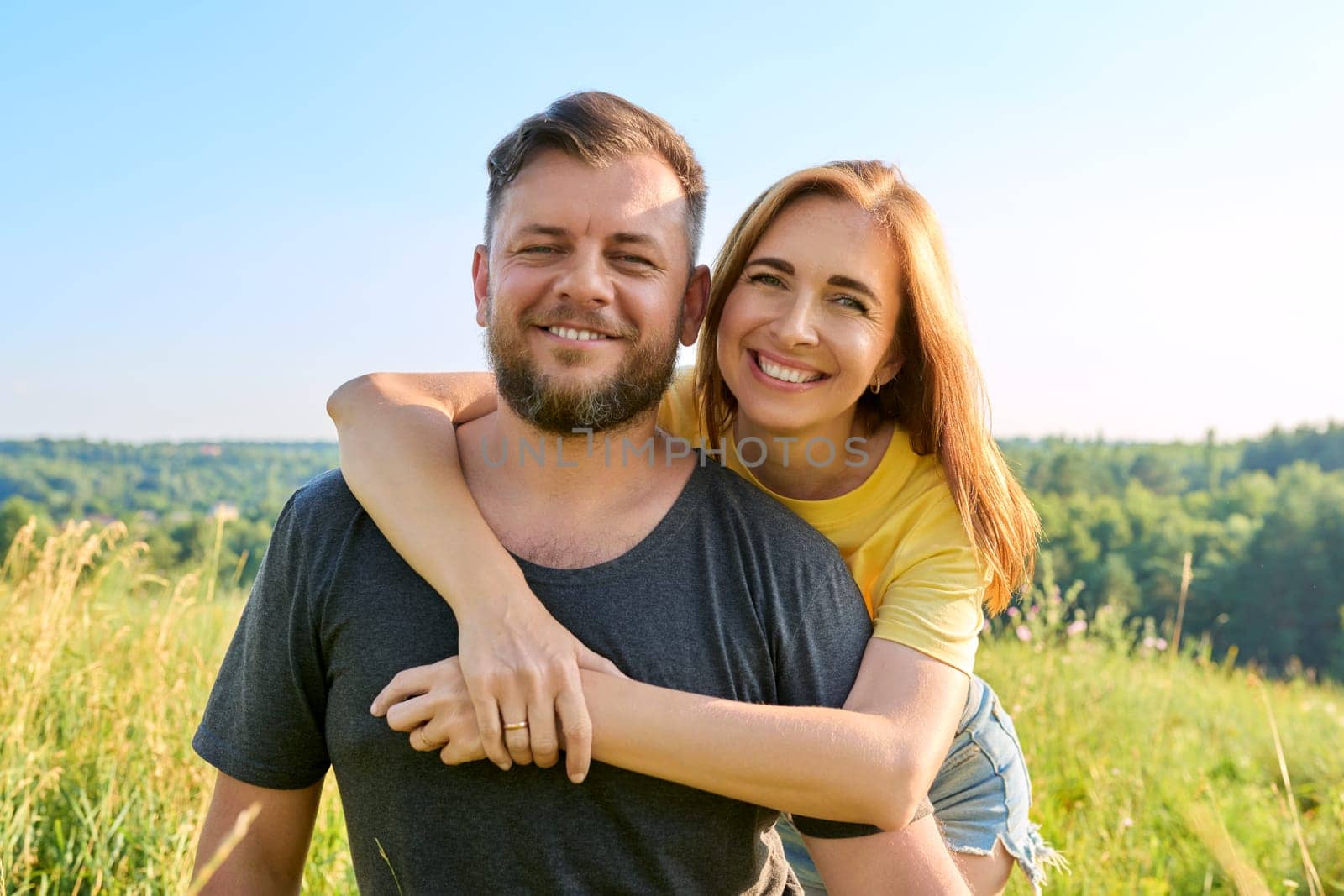 Portrait of happy adult hugging couple on summer sunny day. Beautiful people man and woman embracing in nature, looking at camera, family, happiness, holidays, joy concept