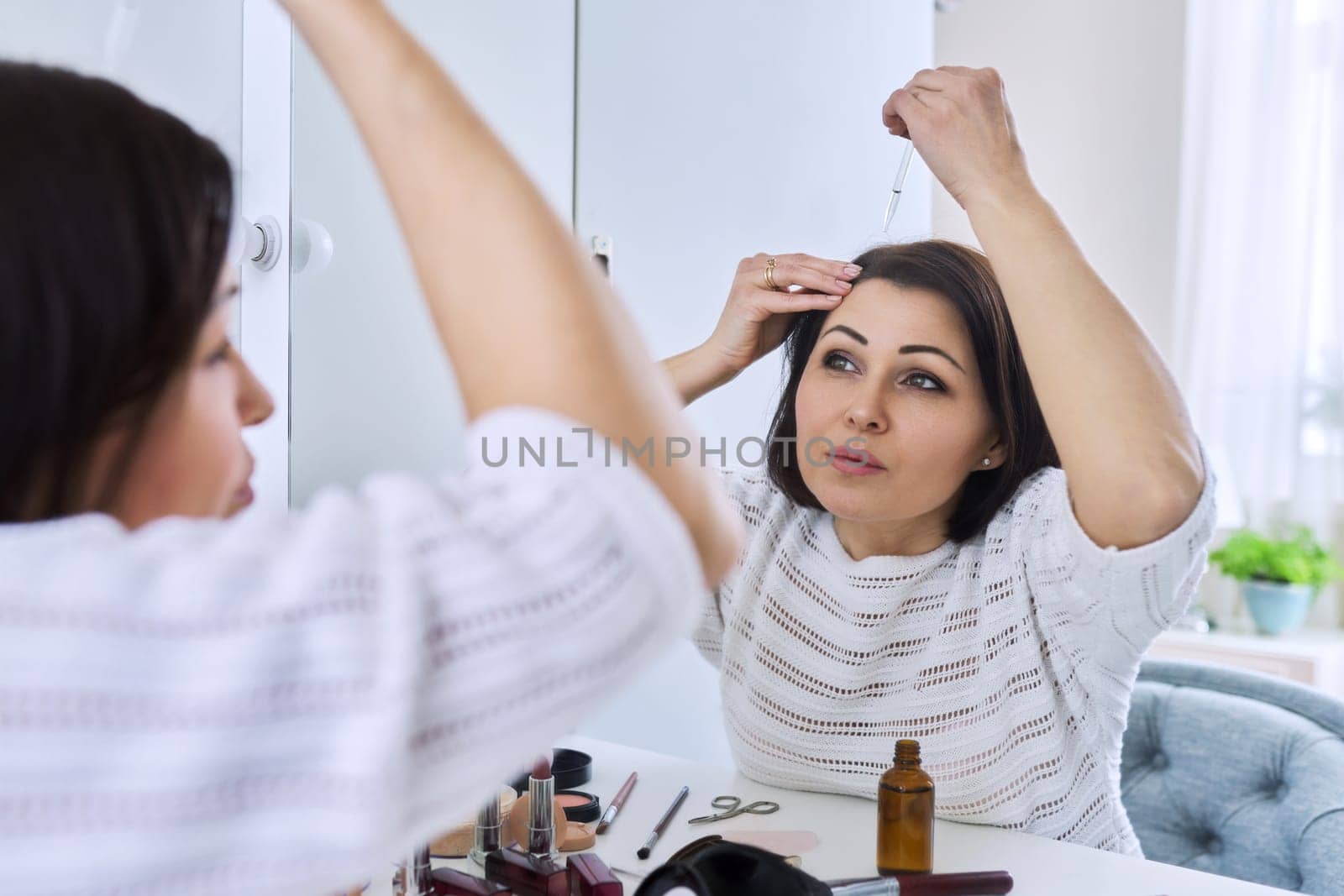 Middle aged woman treating her hair using medical drops. Medicine for care and nutrition of hair, from hair loss