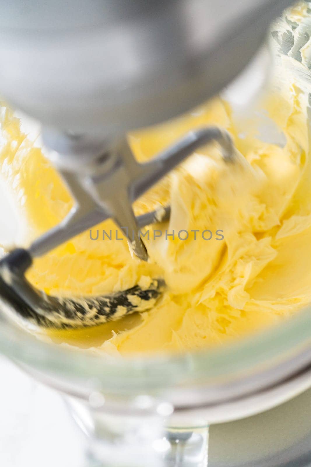 Whisking buttercream frosting in a glass mixing bowl with an electric kitchen mixer for American flag mini cupcakes.