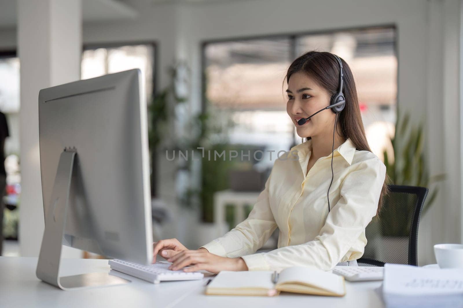 Portrait of happy smiling female customer support phone operator at workplace. Smiling beautiful Asian woman working in call center by nateemee