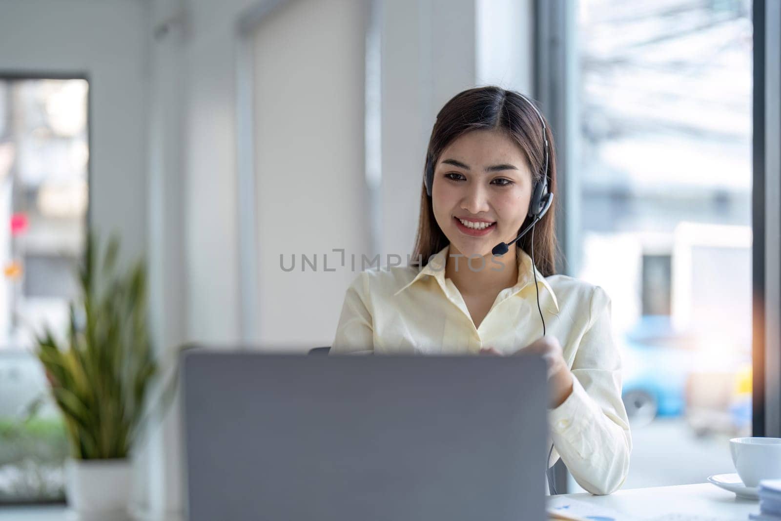 Portrait of happy smiling female customer support phone operator at workplace. Smiling beautiful Asian woman working in call center.