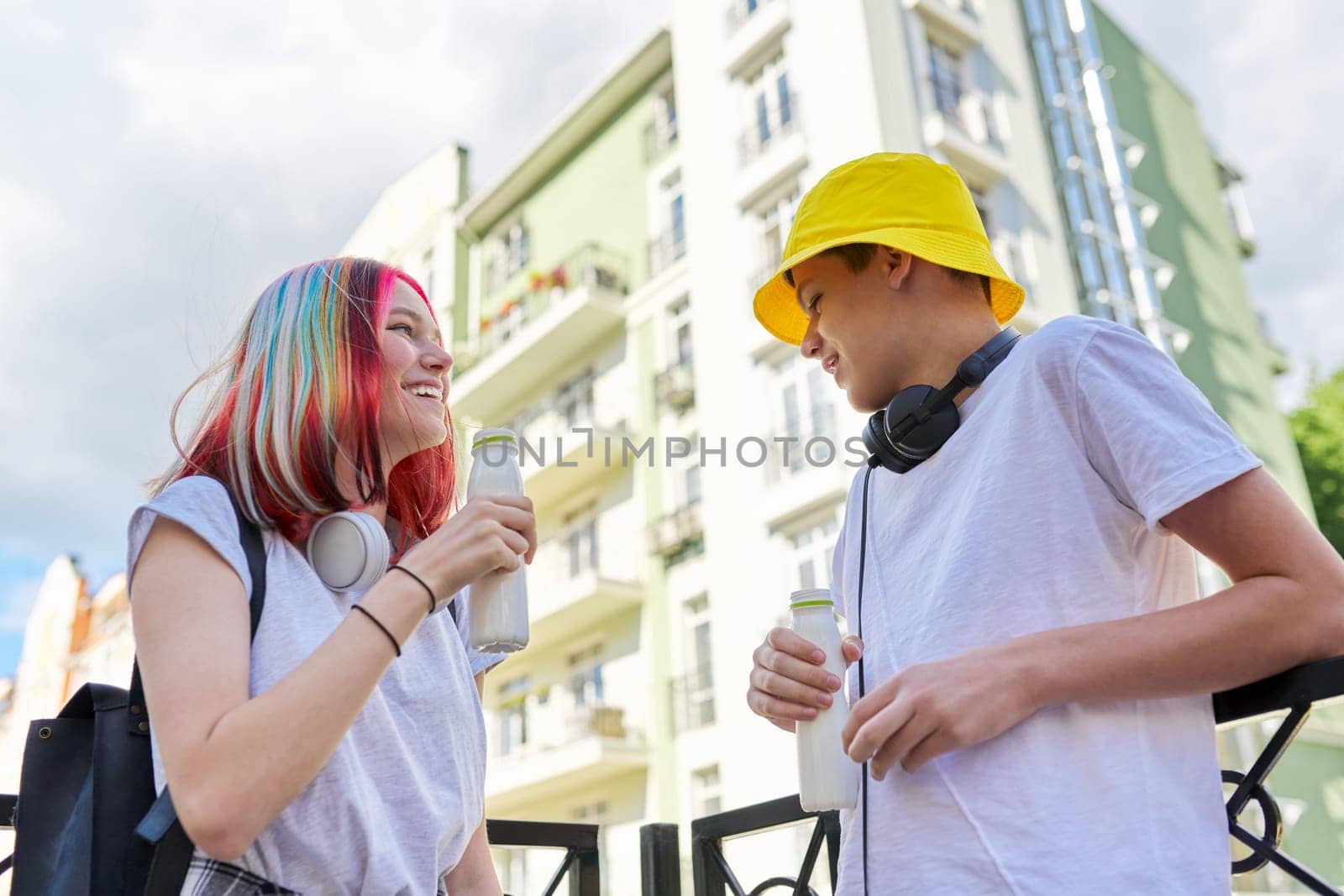 Urban lifestyle of teenagers, couple of college students talking having rest drinking milk drink in bottle outdoors, city street background. Healthy food, youth, recreation and communication concept