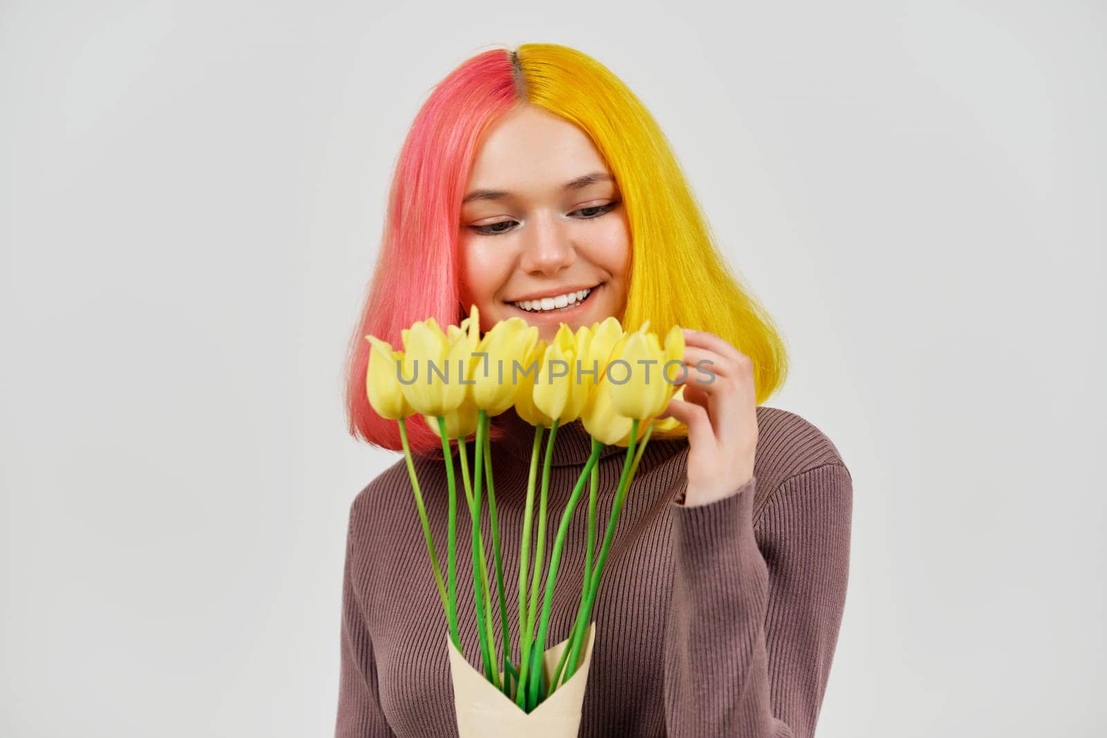 Happy smiling teenager girl with bouquet of yellow tulips on light background close-up. Holiday, spring, joy, happiness, love concept