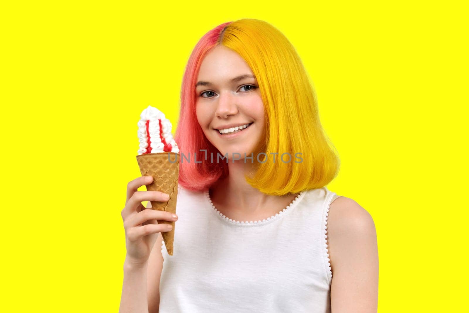 Smiling happy beautiful model teenager with ice cream in waffle cone over yellow studio background. Summer, food, beauty and fashion concept