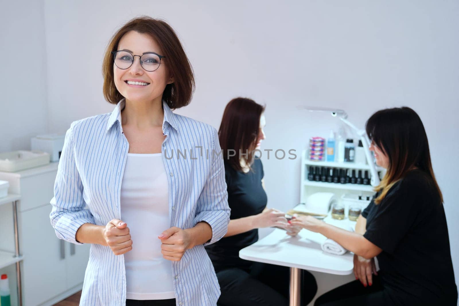 Confident mature woman beauty salon owner taking care of body with hands nails. Smiling female looking at the camera, manicure process background