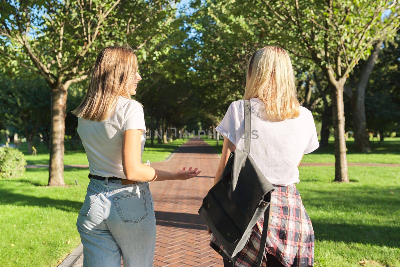 Two happy smiling talking girls teenagers students walking together, back view by VH-studio