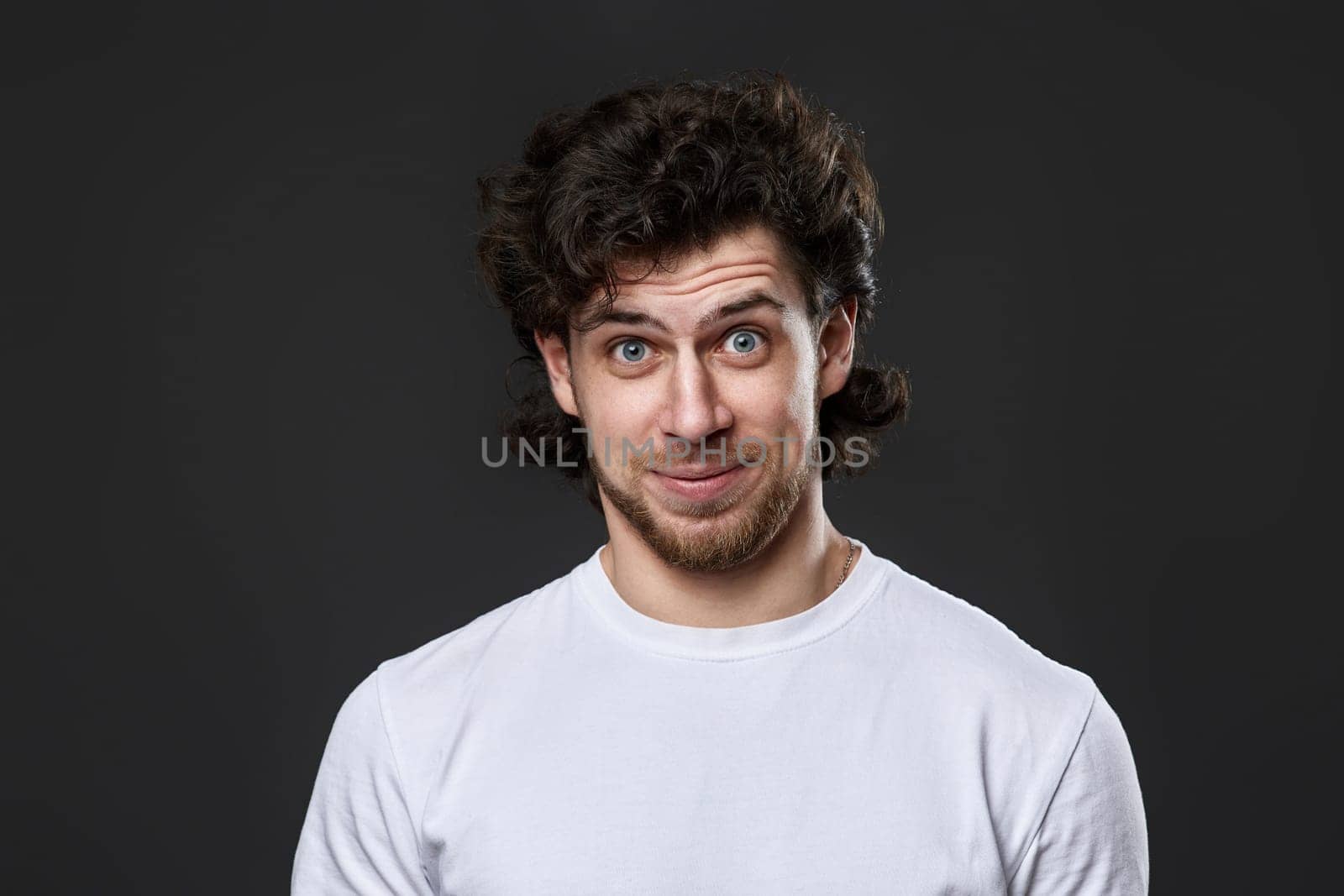 puzzled young bearded man in casual white t-shirt looking at the camera on dark gray background. great idea