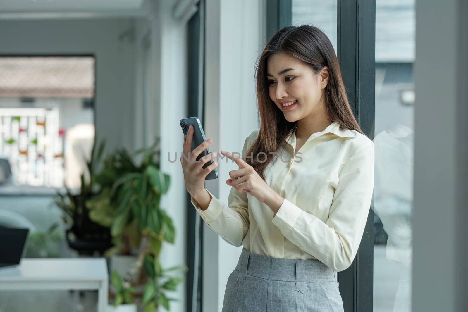 Smiling beautiful Asian businesswoman analyzing chart and graph showing changes on the market and holding smartphone at office