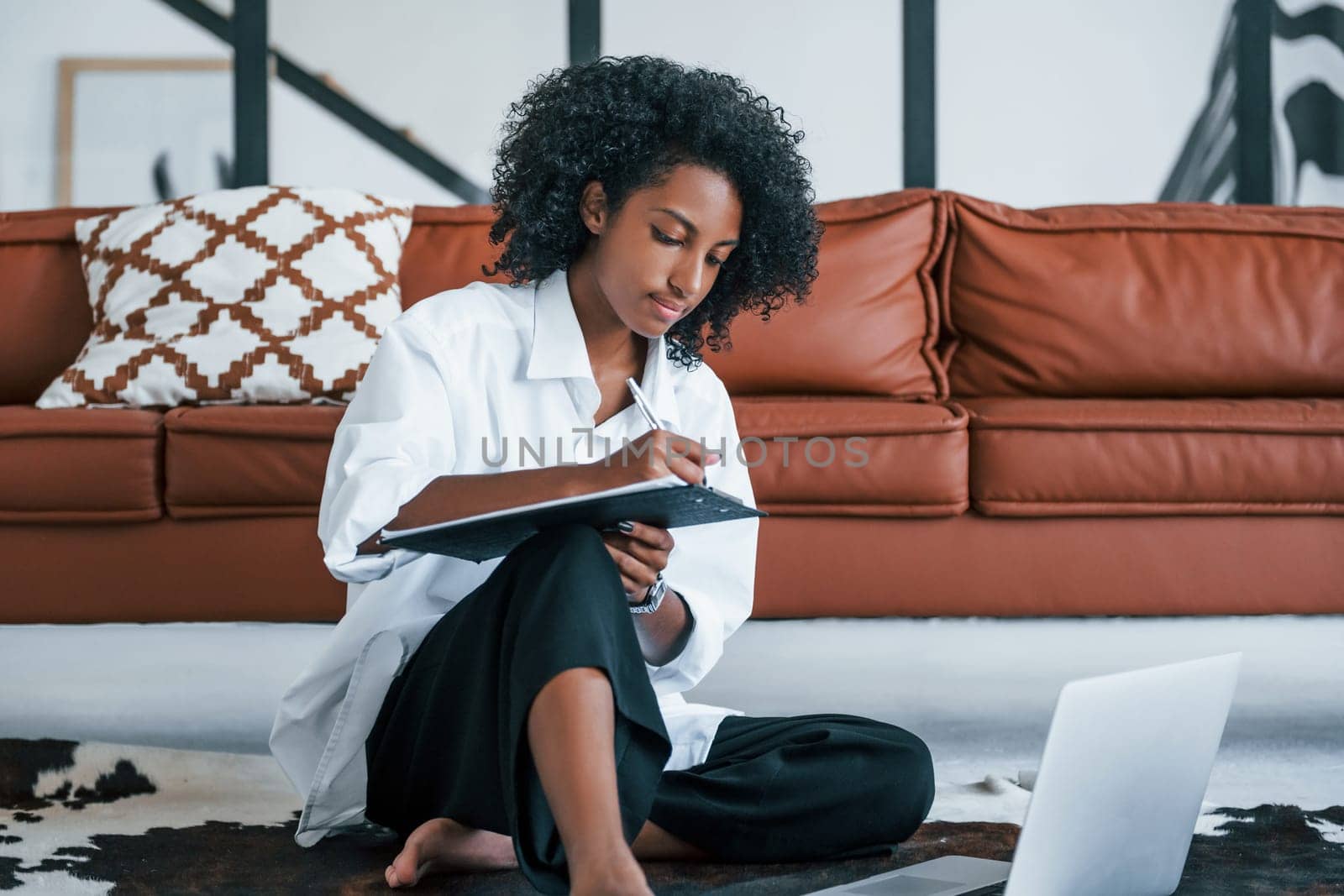 With laptop. Young african american woman with curly hair indoors at home.