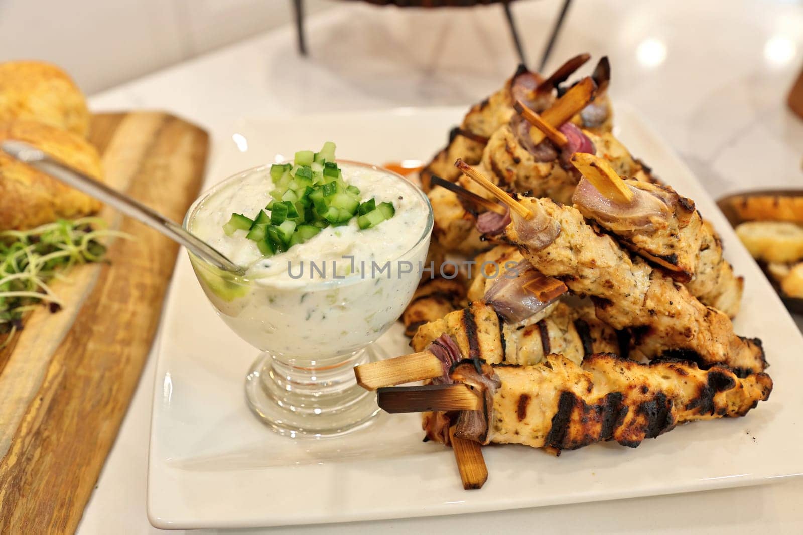 Greek chicken souvlaki skewers or kebabs piled high on a white plate with a bowl of tzatziki sauce by markvandam