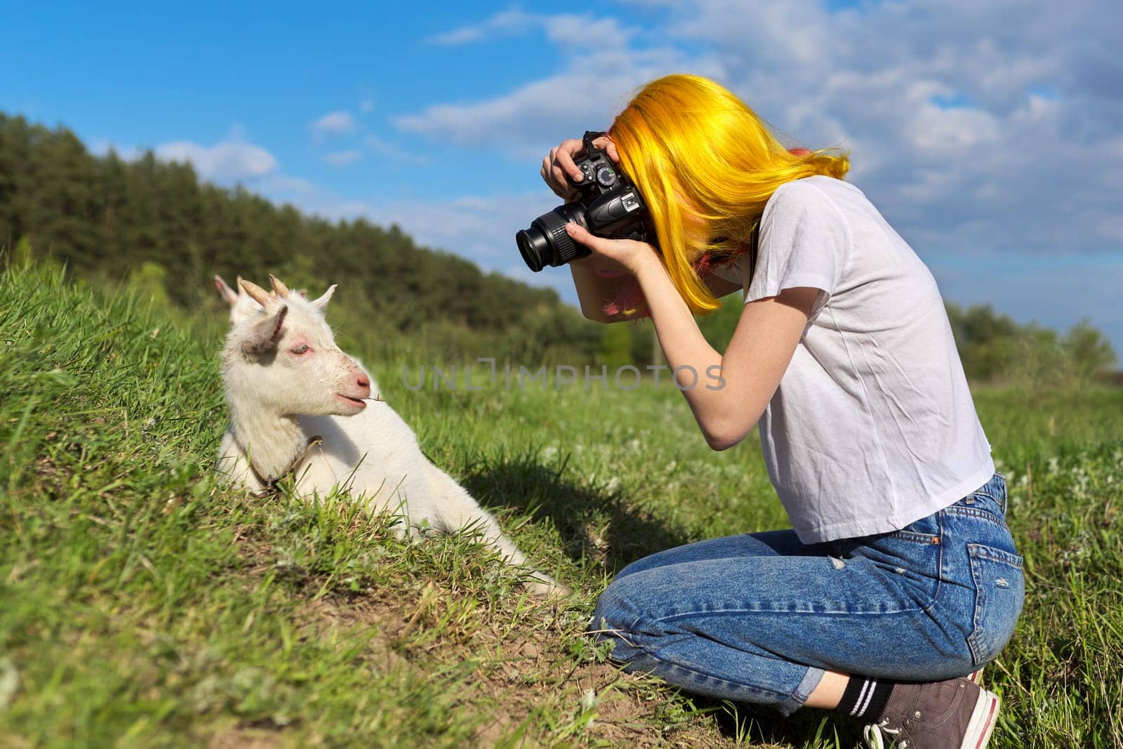 Girl hipster teenager with camera on farm in meadow makes photo of little young goat