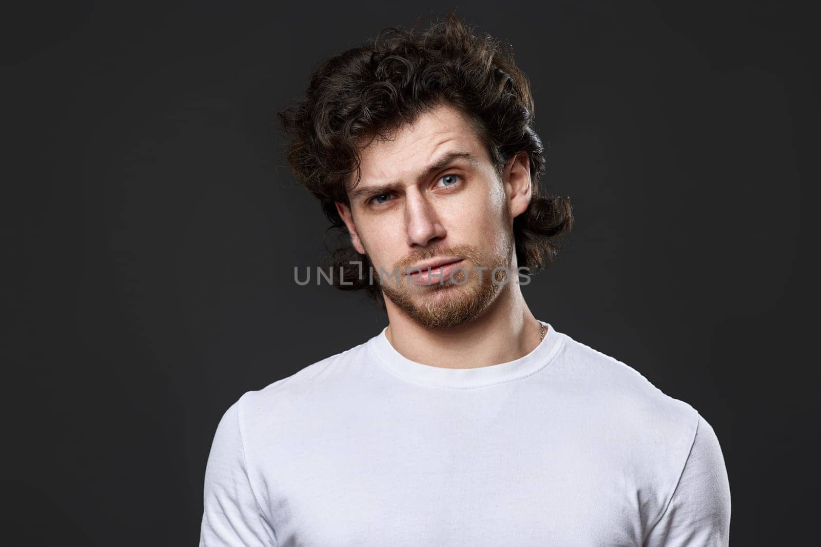 puzzled man in white t-shirt looking suspicious on dark gray background