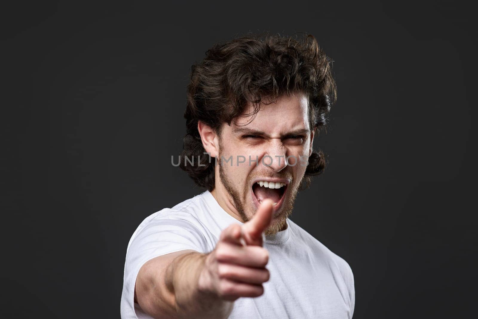 frustrated caucasian man pointing finger at you and the camera on dark gray background