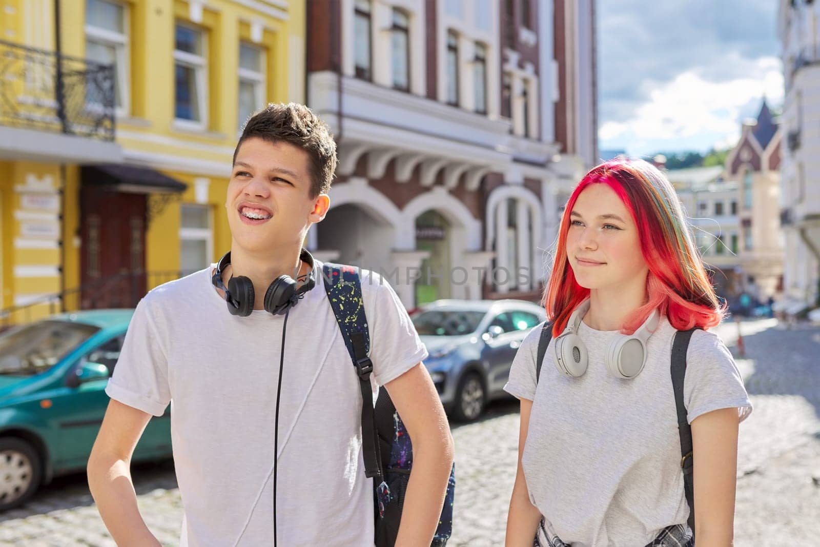 Youth, teenagers, lifestyle, portrait of smiling happy teenage boy and girl college students with backpacks, headphones in sunny city on the street