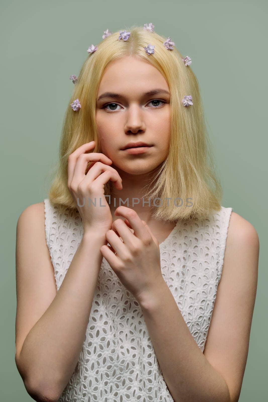 Young tender girl teenager with lilac flowers in blond hair on green background. Beauty, youth, fashion, nature, spring concept