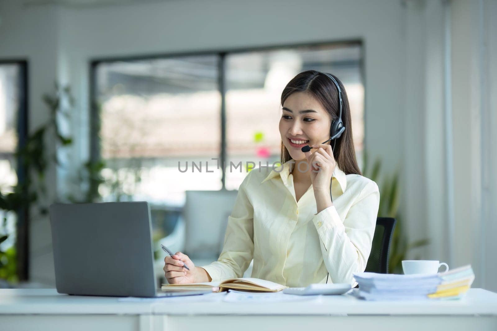 close up call center operator in wireless headset talking with customer, woman in headphones with microphone consulting client on phone in customer support service, looking at computer screen. by wichayada