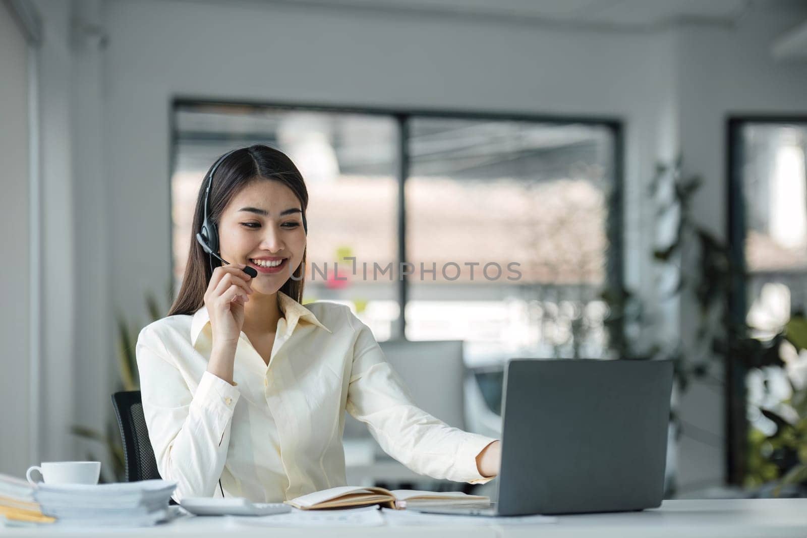 close up call center operator in wireless headset talking with customer, woman in headphones with microphone consulting client on phone in customer support service, looking at computer screen. by wichayada