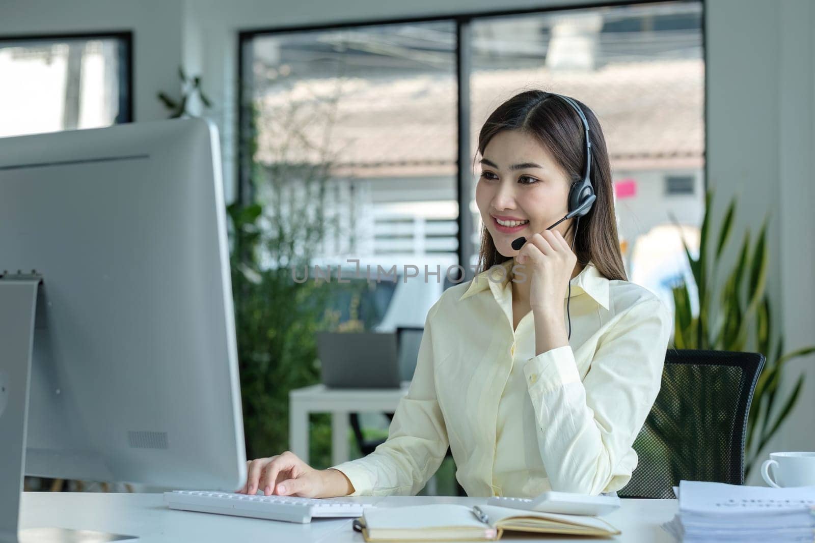 close up call center operator in wireless headset talking with customer, woman in headphones with microphone consulting client on phone in customer support service, looking at computer screen. by wichayada