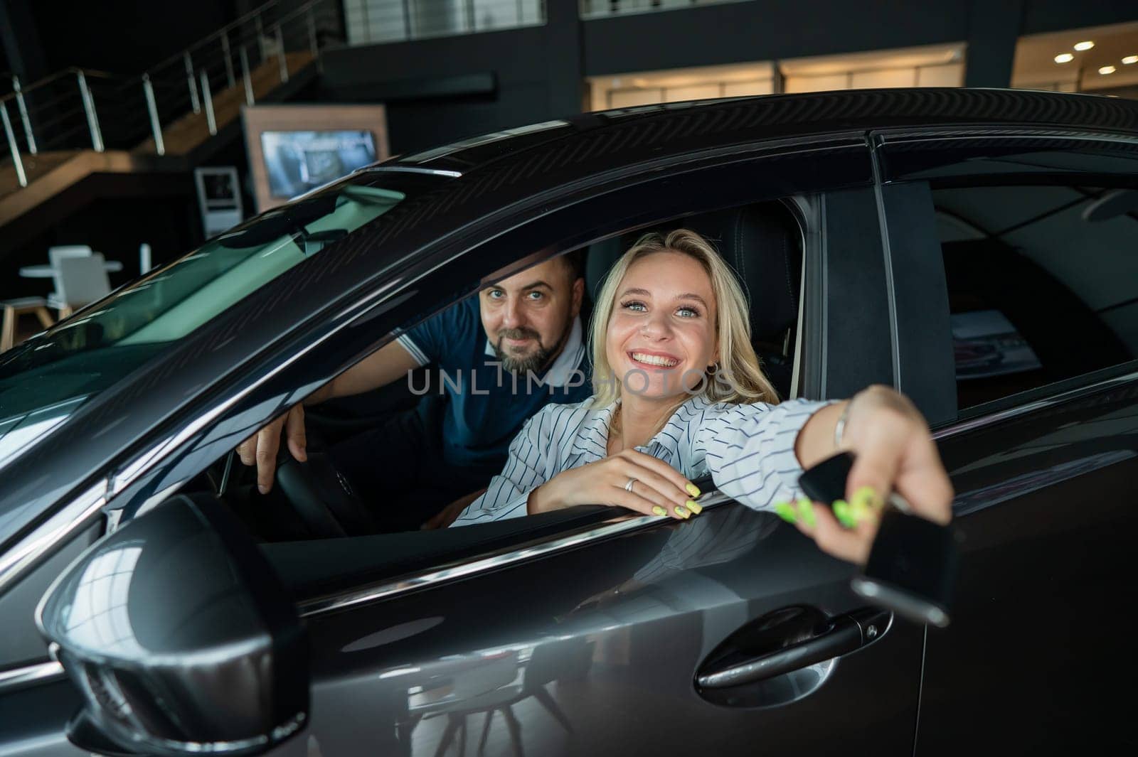 Happy caucasian couple is sitting in a car in a car dealership. A woman holds the keys to a new car. by mrwed54