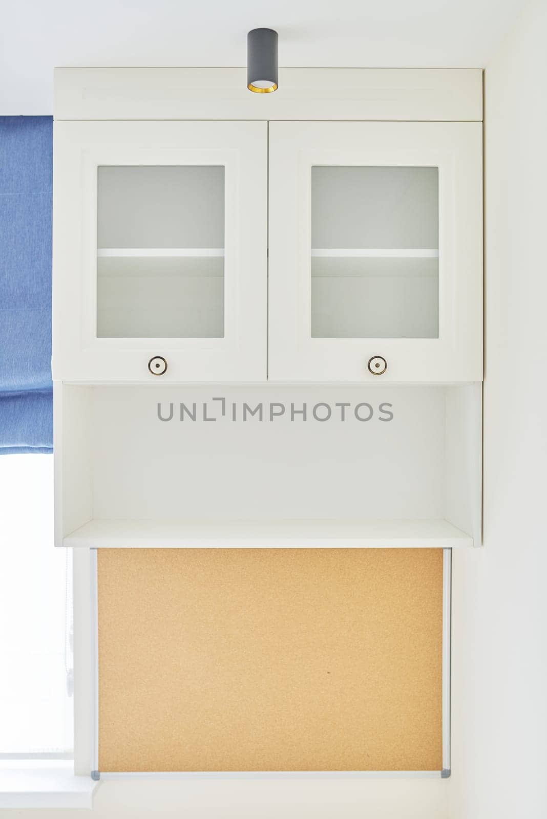 White furniture in the interior, empty open shelf and bookcase with glass door, cork board under the shelf