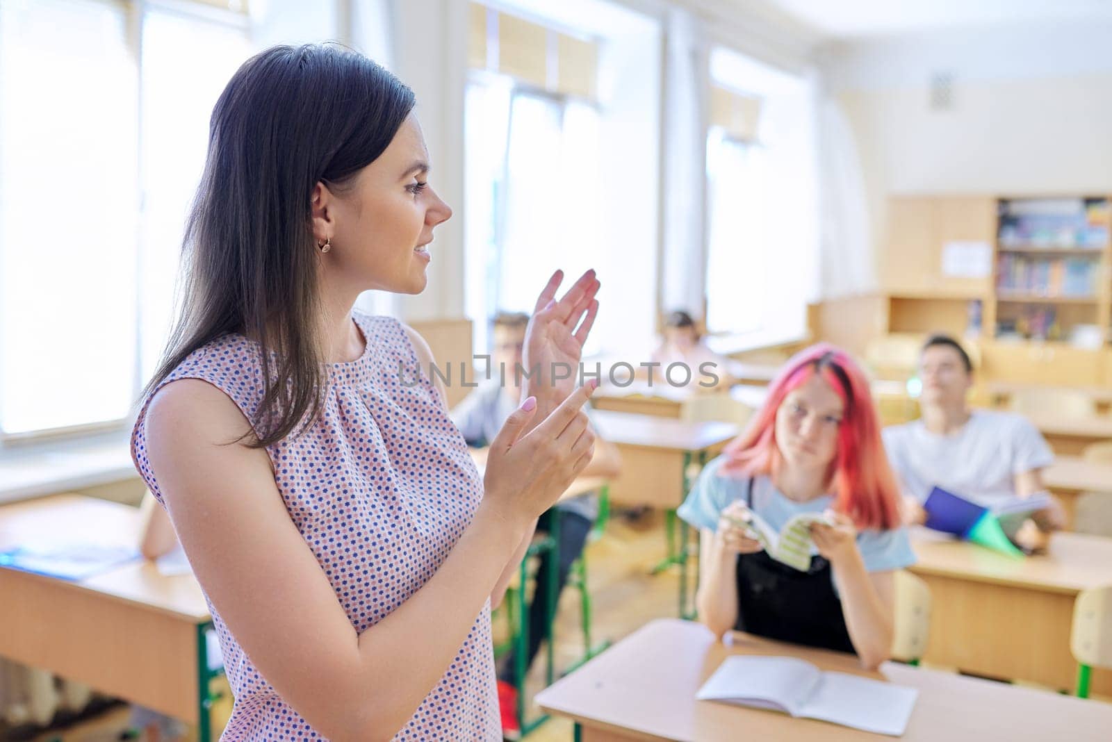 Portrait of young female high school teacher at lesson. Talking female teacher in class with teenage students