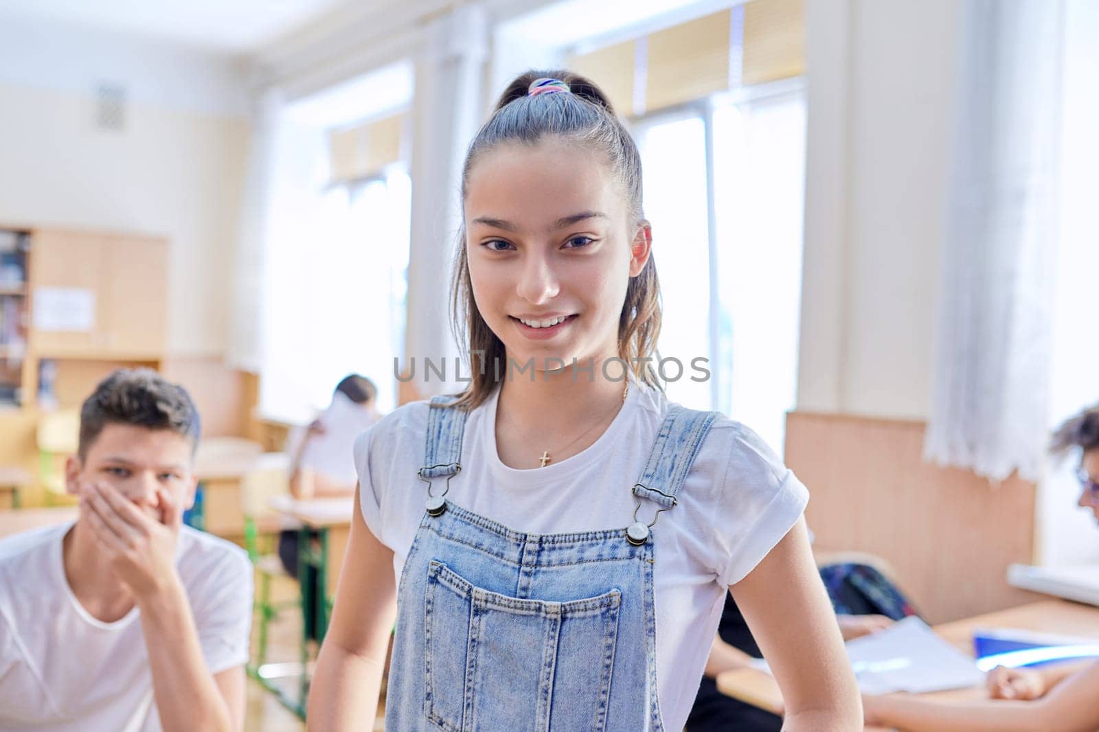 Teenage student taking exam, talking looking at camera, classroom with study students background. School, education, youth concept