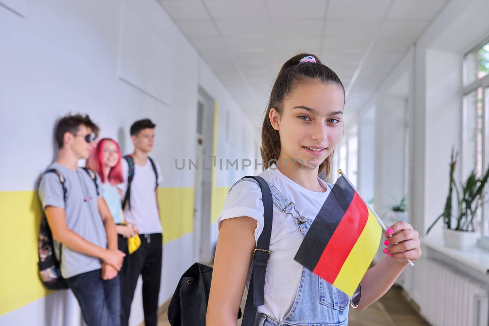 Student teenager girl with the flag of Germany inside school, school children group background. Europe, Germany, education and youth, patriotism, people concept