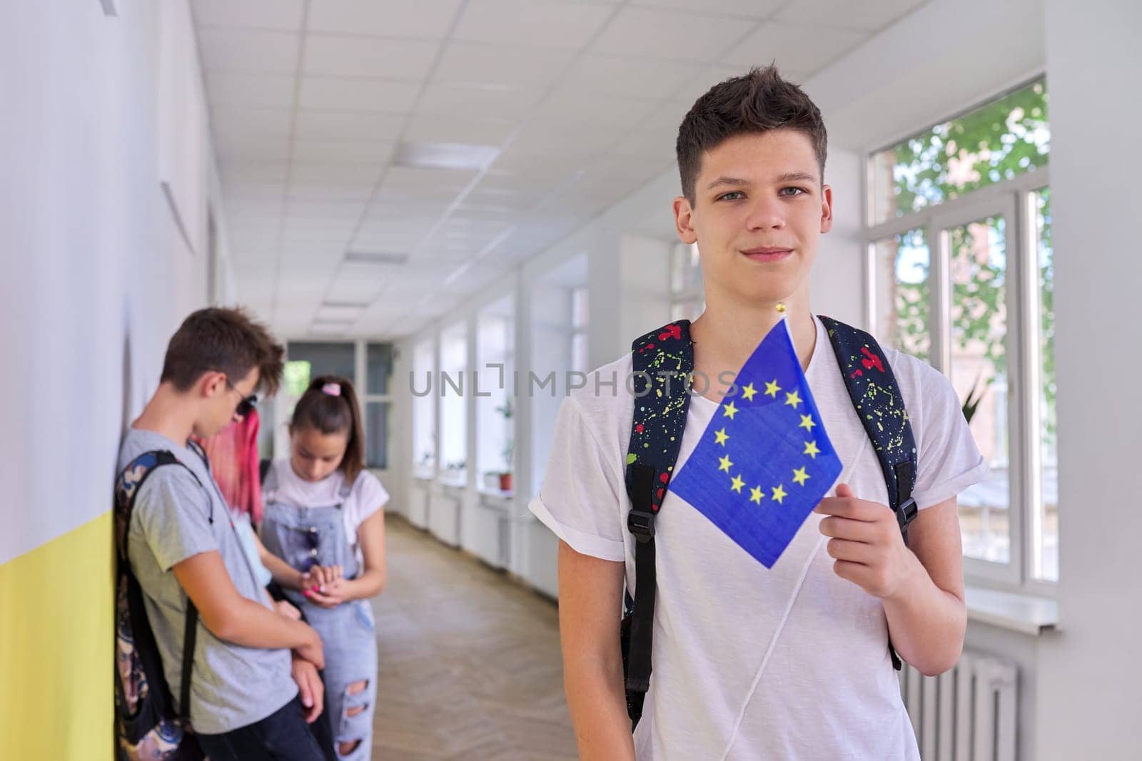 Male student teenager with EU flag inside college, group of students background. European Union, education In Europe, young people concept