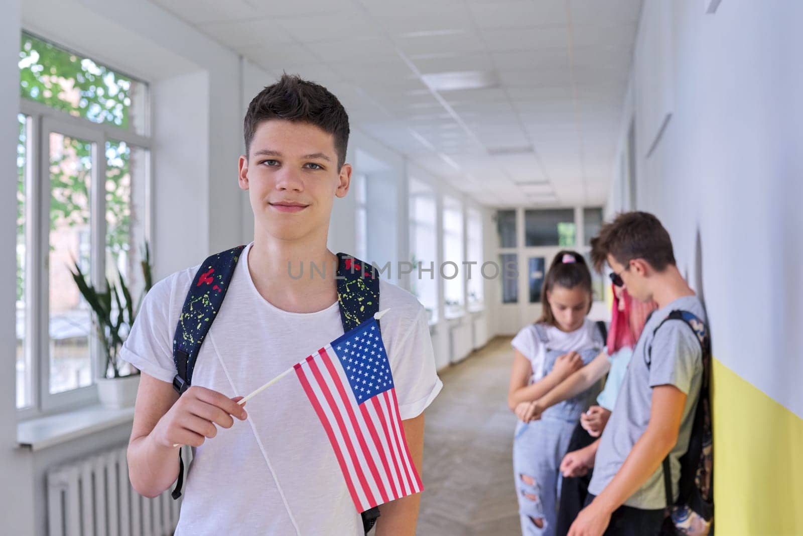 Male student teenager with USA flag inside college, group of students background by VH-studio