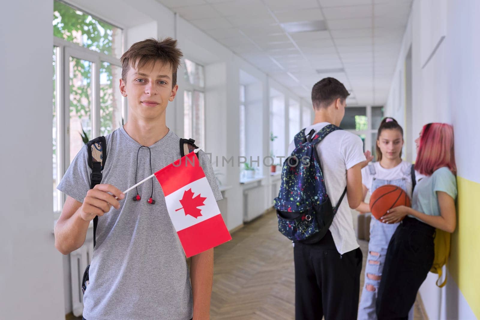 Student teenager male with flag of Canada inside school, children group background. Canada, education and youth, patriotism, people concept