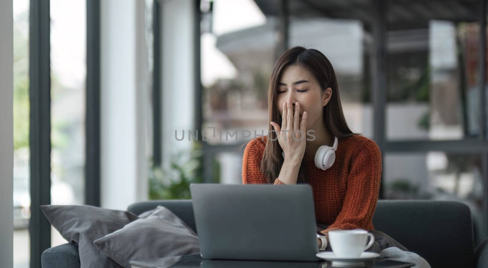 asian young woman listening music with headphone and streaming music from laptop on sofa relaxing at home..